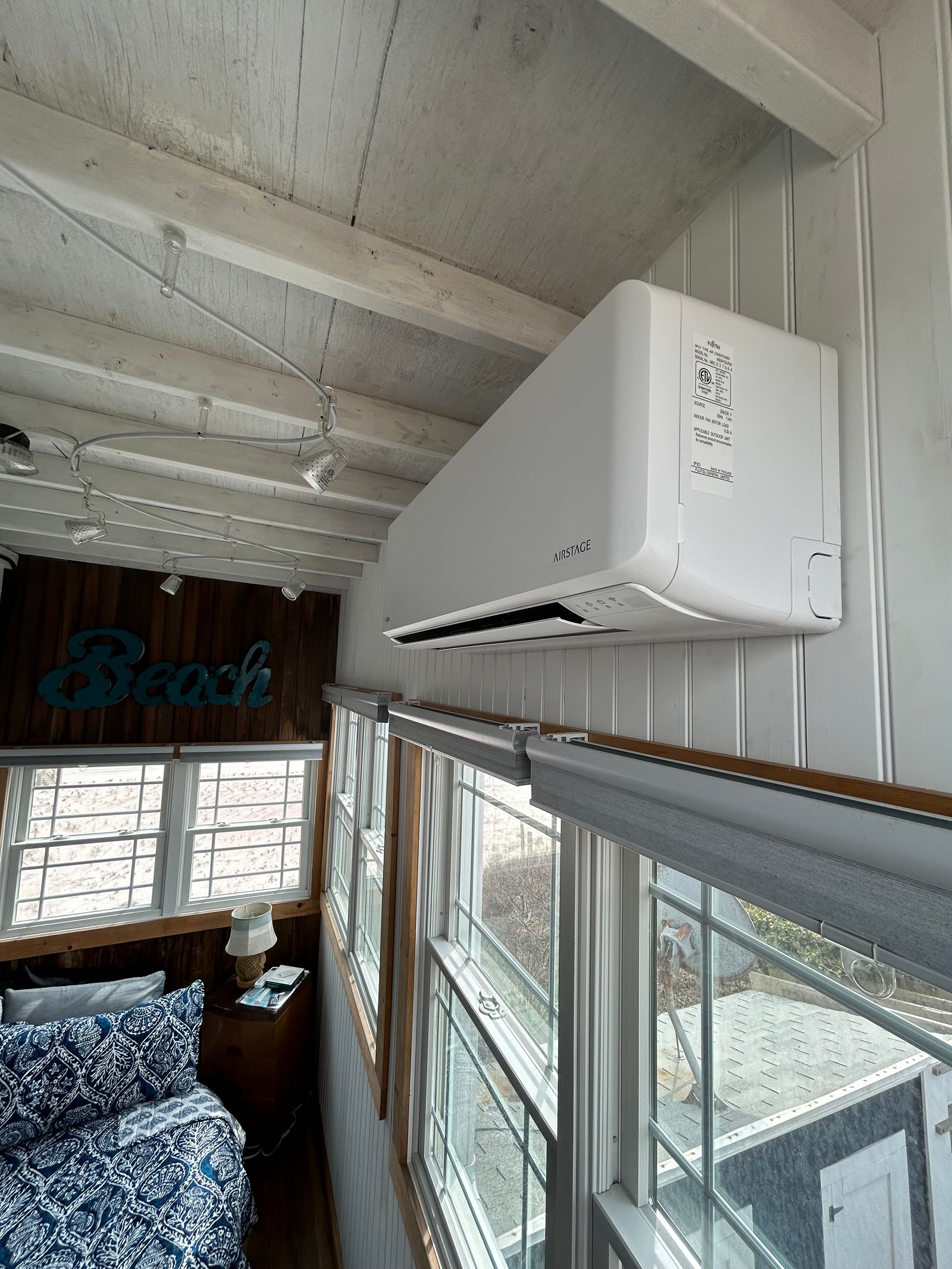Airstage mini-split indoor unit installed in a coastal-style bedroom with exposed wooden beams and large windows overlooking an outdoor area.