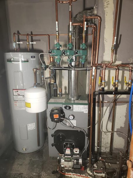 Boiler system with copper piping, circulator pumps, and an A.O. Smith water heater installed in a basement.