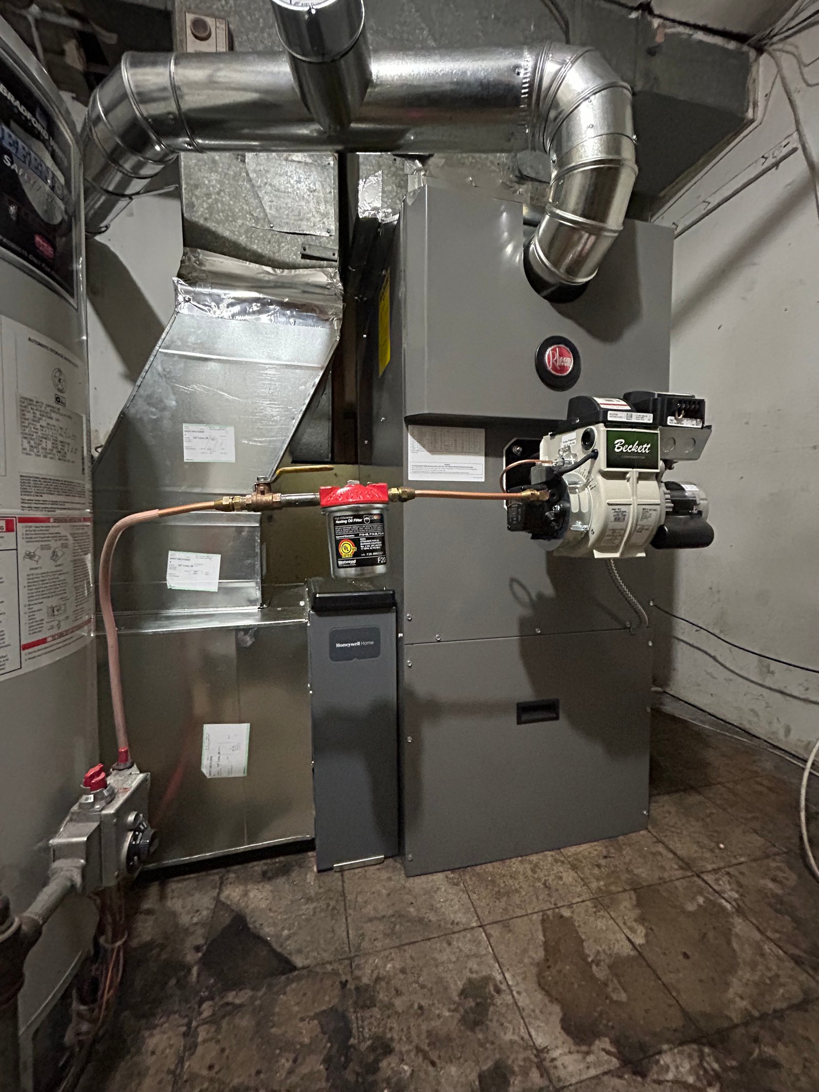 Rheem oil furnace installed in a basement with galvanized ductwork, a Beckett burner, and a connected water heater, ensuring efficient heating and HVAC performance.